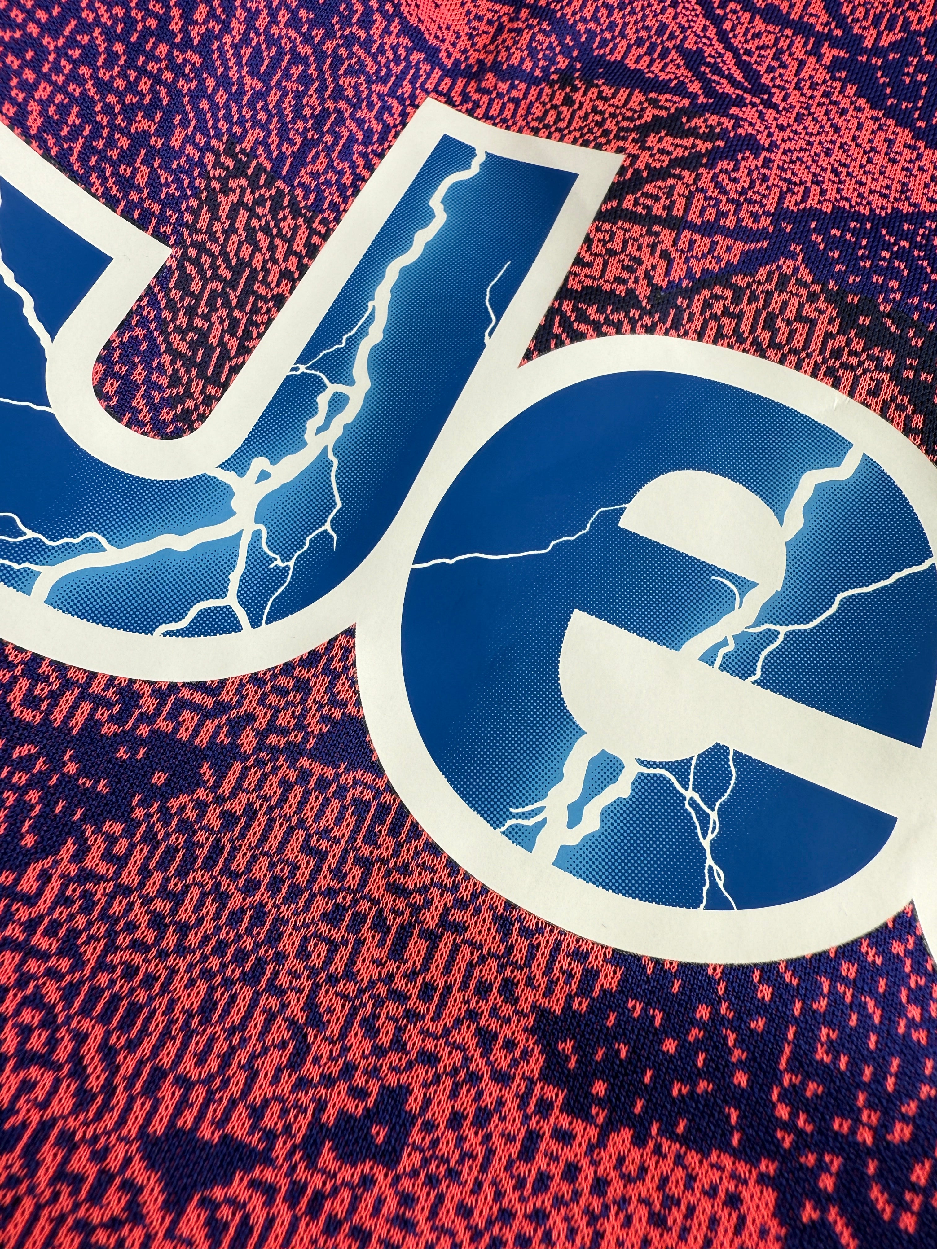 Blue and white symbol with lightning effects on a red and blue patterned background.