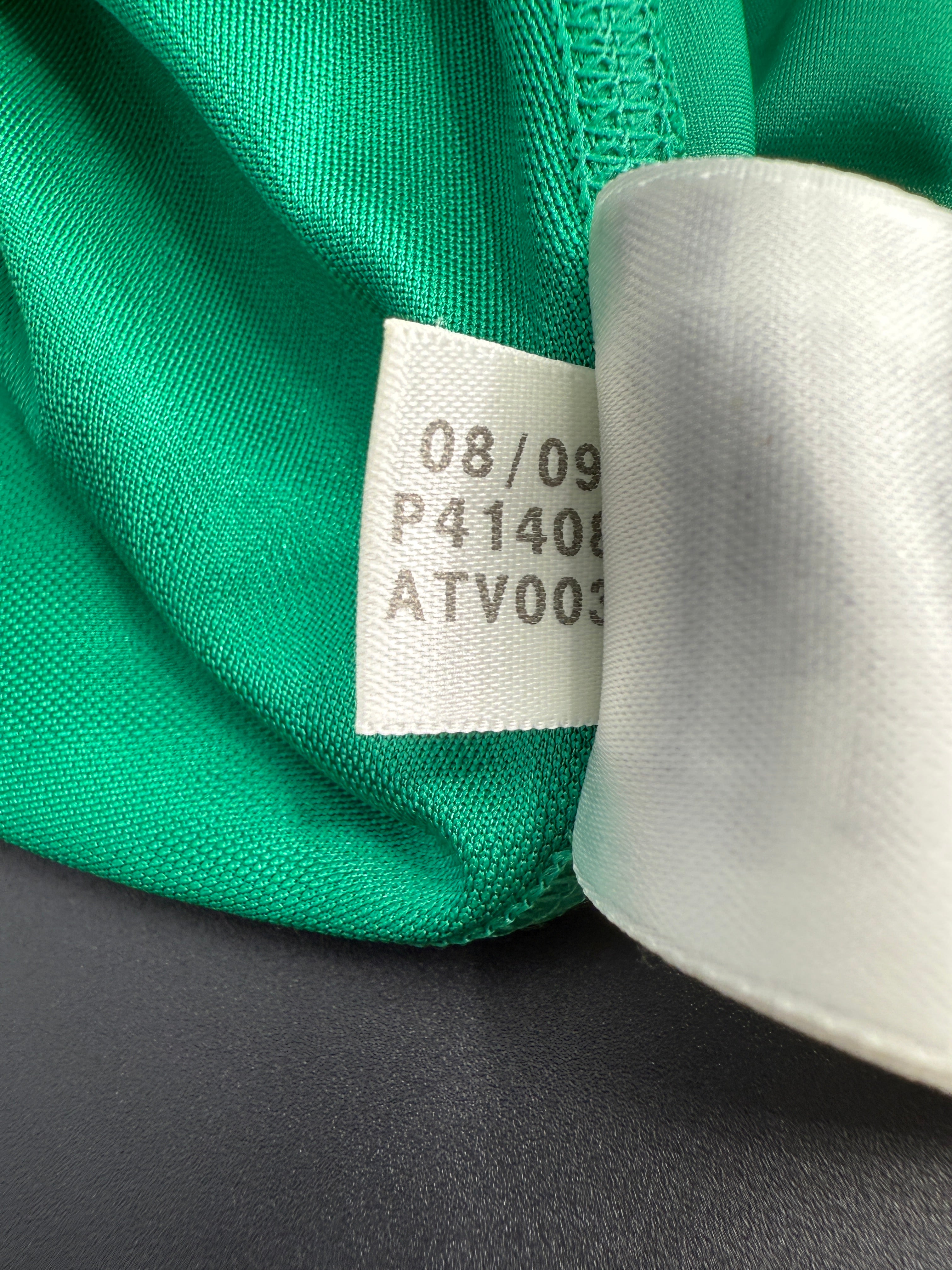 Close-up of green fabric with a label and spool of white thread.
