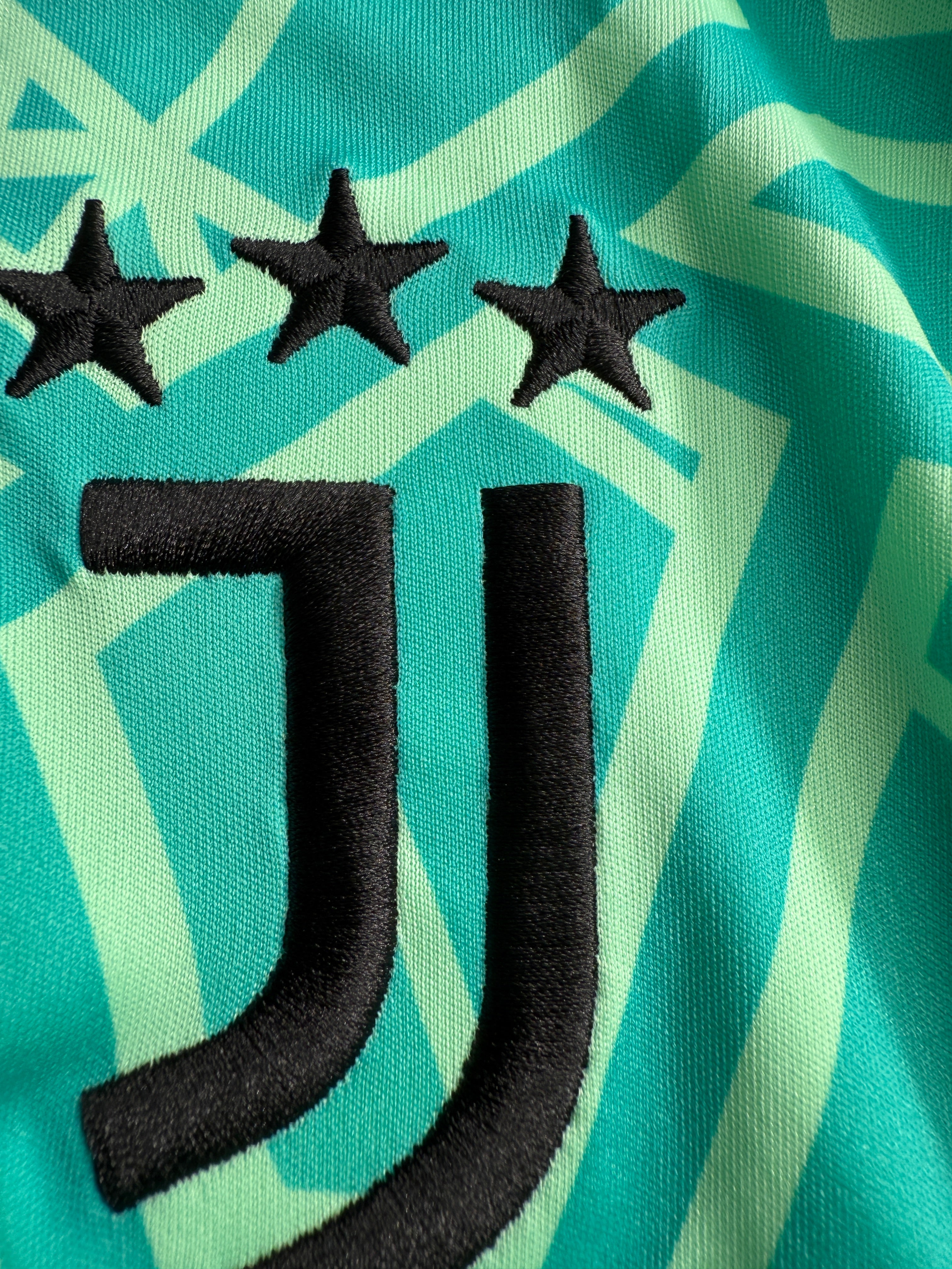 Close-up of black star and crescent shape embroidery on teal fabric.