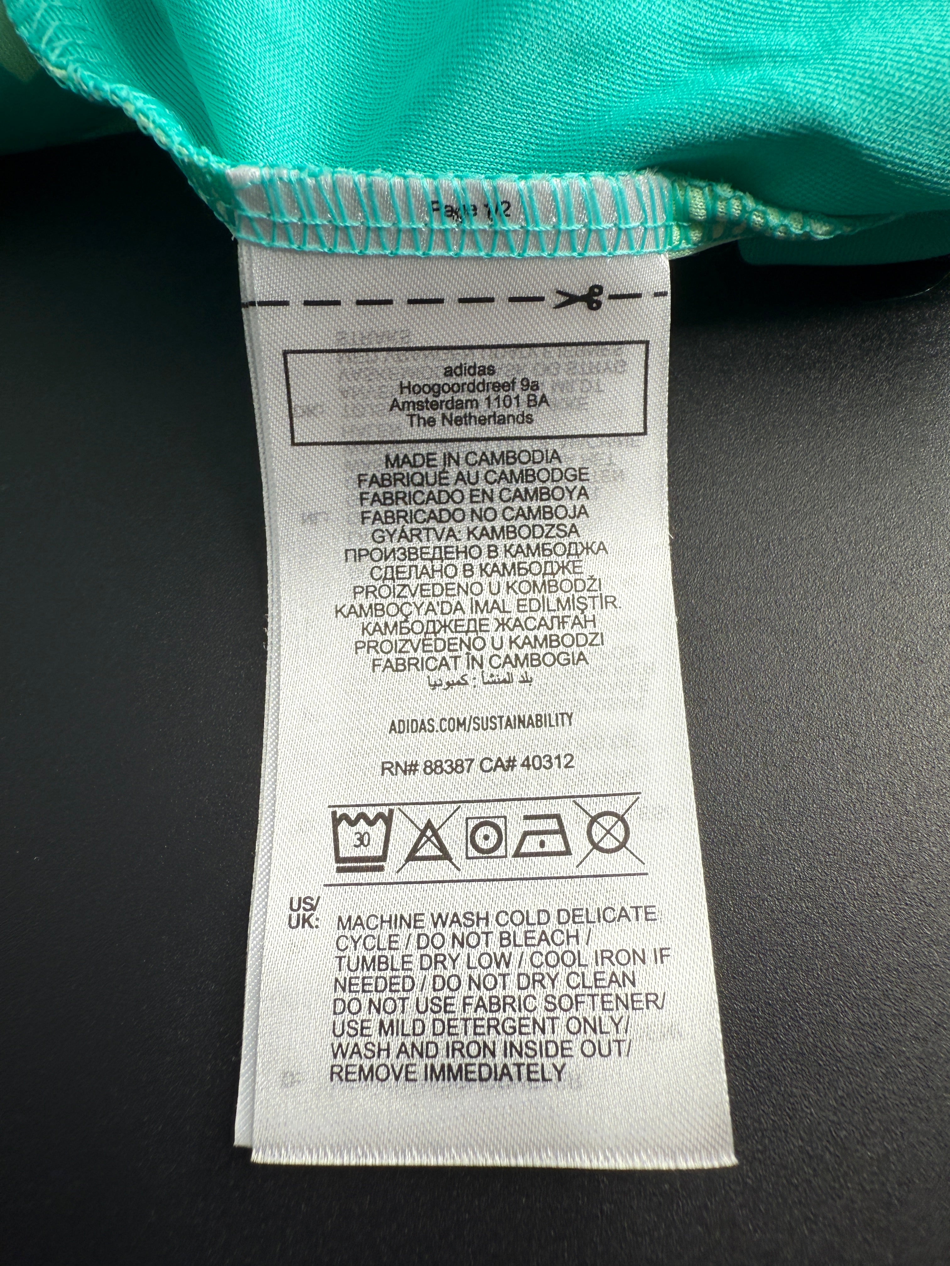 Close-up of a fabric label on a teal garment against a dark background.